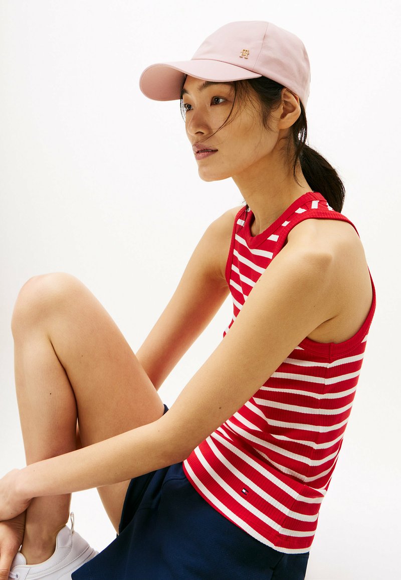 Top senza maniche a righe rosse e bianche con texture a costine, abbinato a una gonna blu navy e un cappellino rosa chiaro con un piccolo logo.