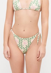 Bikini komplekts ar zaļu un bēšu ziedu rakstu, ar trīsstūra blūzi un regulējamiem sānu saitēm. Gluda, stiepjama auduma.