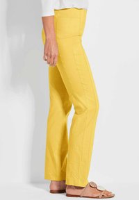 Gele katoenen broek met rechte benen, voorzien van opvallende stiksels, zijzakken en een soepele textuur. G gedragen met beige sandalen.