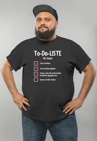 Schwarzes T-Shirt mit weißem Text und Kästchen für eine To-Do-Liste. Das Design enthält verspielte Phrasen auf Deutsch. Lässige Passform, kurze Ärmel.