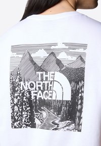 Mountain landscape graphic with pine trees, river, and text "THE NORTH FACE" on the back of a white shirt.