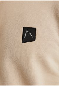 Fascia quadrata nera con design astratto a linee bianche cucita su tessuto lavorato a maglia beige.