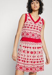 Vestido tricotado vermelho e branco com decote em V, sem mangas, e padrões decorativos de estrelas, corações e cogumelos. Cintura elástica.