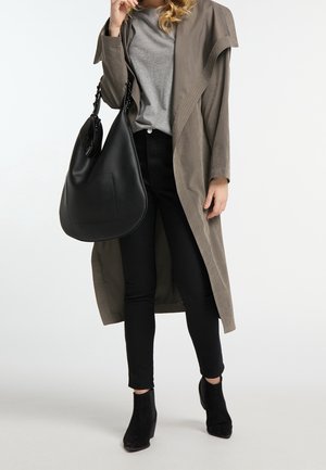 Manteau trench gris oversize sur un t-shirt gris, jeans skinny noirs et bottines noires à cheville, tenant un sac hobo en cuir noir avec une poche plate.