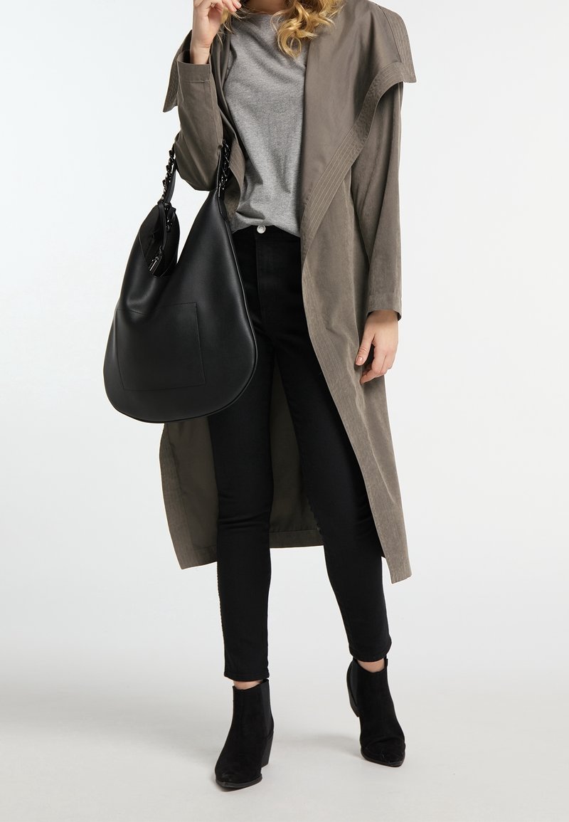 Grå overdimensioneret trenchcoat over en grå t-shirt, sort skinny jeans og sorte ankelstøvler, mens der holdes en sort læder hobo taske med en flad lomme.