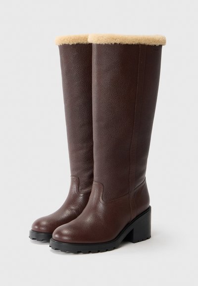 Brown leather knee-high boots with a soft beige fur trim, block heel, and textured surface; rubber sole with traction detail.