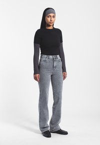 Top negro de manga corta con mangas largas grises, combinado con unos vaqueros de cintura alta de color gris claro. Modelo lleva zapatos negros y una cinta para la cabeza gris.