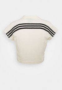 Zkrácená krémová polokošile s černými třemi pruhy podél zad a krátkými rukávy, s jemnou texturou a jednoduchým designem.