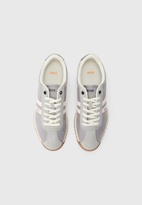 Graue Sneakers aus Veloursleder und Mesh-Materialien, weiße Schnürsenkel, orangefarbene Akzente und eine Gummisohle. Mit Markenlogo auf der Zunge und an der Seite.