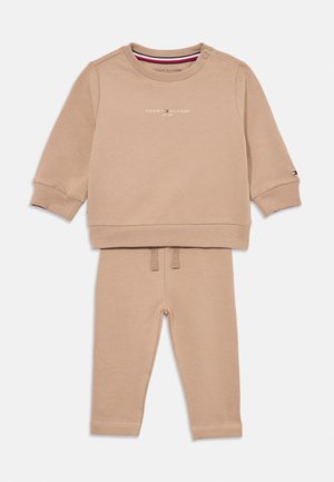Beige Baumwoll-Trainingsanzug mit einem Langarmshirt mit Druckknöpfen an den Schultern, rundem Ausschnitt und passenden Hosen mit elastischem Bund und Knöchelabschlüssen.