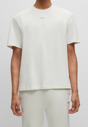 T-shirt beige clair à manches courtes en coton doux, avec un petit logo vert "HUGO" sur la poitrine, coupe décontractée.