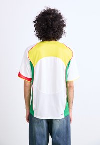 Kortærmet sportsjersey med en hvid bund og gule, grønne og røde accenter. Meshmateriale, afrundet ryg og kontrastsyninger.