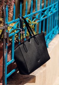 Černá taška přes rameno vyrobená z texturovaného materiálu, s dvěma uchy, v-řezem nahoře a logem vyraženým na přední straně.