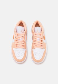 Baskets avec une base en cuir blanc et des accents pêche, présentant un bout perforé, des lacets pêche et un logo de marque orange sur le côté.