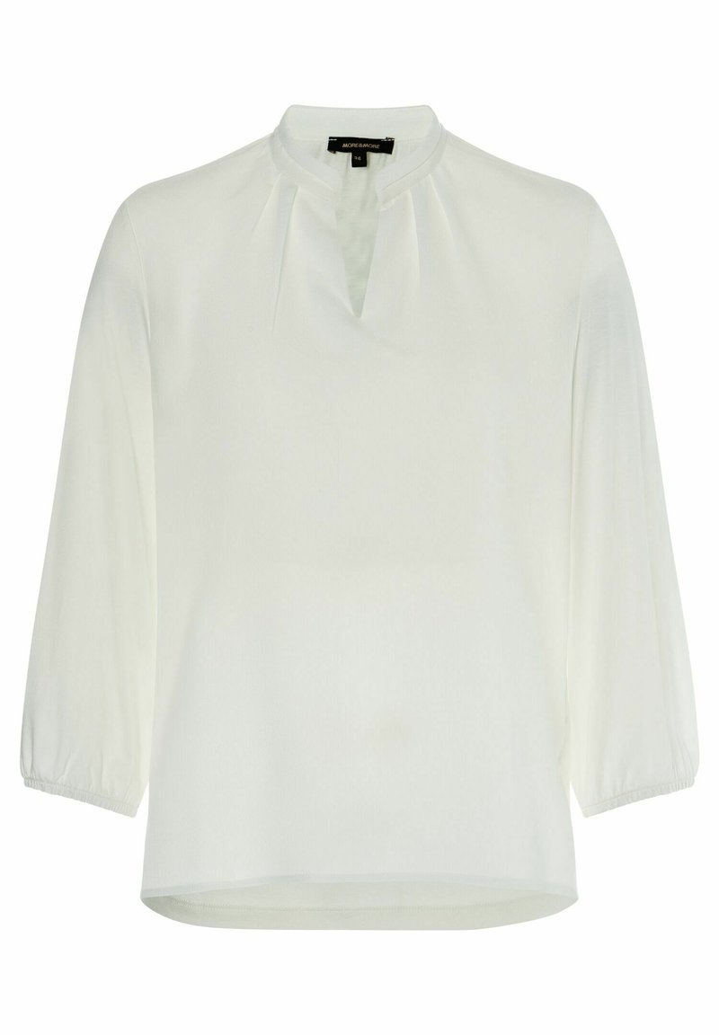 Blouse blanche à manches longues avec un col rond et une petite fente en V, avec de subtils plis près de l'encolure et des poignets élastiques.