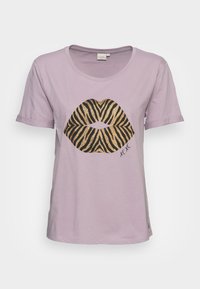 Camiseta de algodón de color púrpura claro con un gran gráfico de labios a rayas en dorado y negro en la parte frontal. Manga corta con dobladillos enrollados.