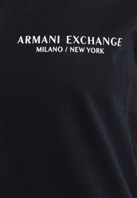 Černé bavlněné tričko s bílým nápisem: „ARMANI EXCHANGE MILANO / NEW YORK.“ Hladká tkanina, střih s kulatým výstřihem, minimalistický styl.