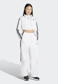 Biely skrátený kabát a nohavicový set vyrobený z ľahkého materiálu s čiernymi bočnými pruhmi. Obsahuje zips a elastický pás.