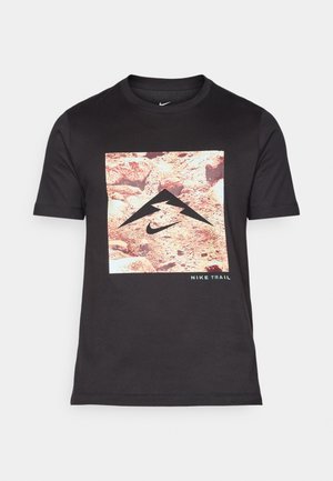 Sort t-shirt med korte ærmer og et rektangulært grafisk design, der viser et klippeområde, et bjerglogo og "NIKE TRAIL" tekst i blå.