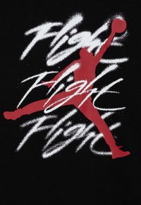 Camiseta negra con una silueta roja de una figura saltando que sostiene un baloncesto, con texto en brochazo blanco que dice "Vuelo Vuelo Vuelo."