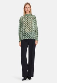 Leichte, durchsichtige Bluse mit einem mintgrünen und navyblauen geometrischen Muster, hohem Kragen und elastischen Bündchen, kombiniert mit navyblauen Hosen.