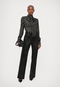 Black blouse with white polka dots, tie at the neck. High-waisted black pants, wide-leg cut, textured fabric. Black heels and handbag.