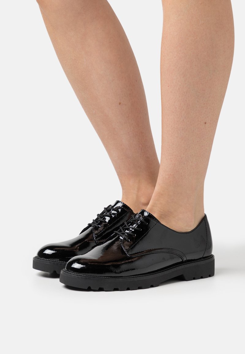 Scarpe in pelle verniciata nera con una finitura liscia, punta rotonda e suola in gomma spessa. Presentano lacci e dettagli di cucitura sottili.