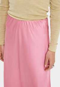 Lichtroze satijnen rok met een gegatherde tailleband, gecombineerd met een beige lange mouwen top. Gladde textuur, middellange ontwerp.
