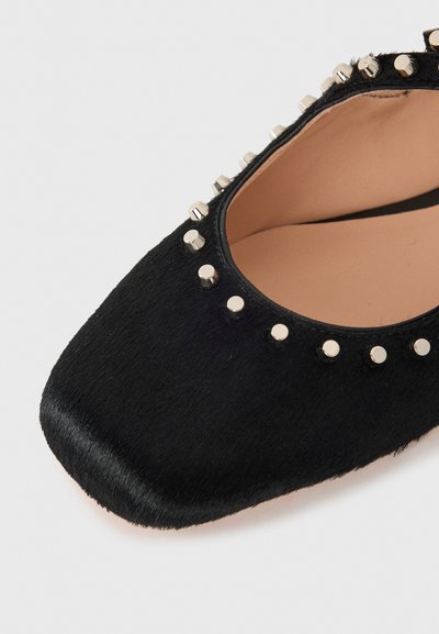 Chaussure noire à bout carré, fabriquée en matériau doux et texturé, ornée d'accents en clous métalliques le long de l'ouverture. Dotée d'une doublure intérieure lisse.