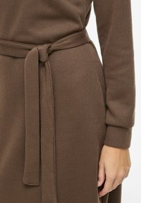 Brązowa sukienka prążkowana z wiązanym paskiem w talii, miękką fakturą, długimi rękawami i dopasowanym krojem podkreślającym sylwetkę.