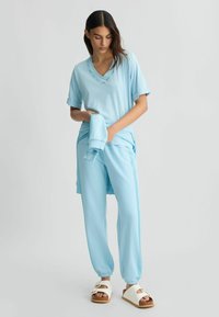 Completo sportivo azzurro chiaro composto da una maglietta a maniche corte con scollo a V, pantaloni aderenti coordinati con cintura regolabile e sandali bianchi.