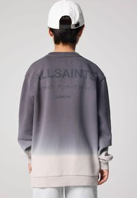 Svetrová mikina s šedobielym gradientom a logom "ALLSAINTS" na chrbte, s rebrovanými manžetami a vo voľnom strihu. Hladká textúra, ležérny dizajn.