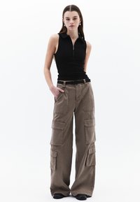 Haut sans manches noir avec un col zippé, associé à un pantalon cargo large en kaki avec de nombreuses poches et passants de ceinture.