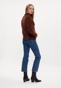 Brun cordfløjljakke, tætsiddende design, to knapper, rygstykke detaljer. Kombineret med blå lige ben jeans og sorte hæleboots.