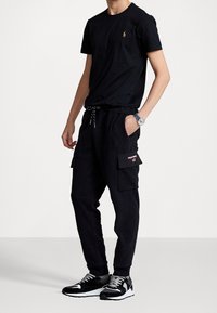 Svart bomull t-shirt med en liten guldlogotyp, kombinerad med svarta cargo sweatpants med fickor och röd logotyp, avslutad med svarta sneakers.