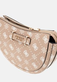 Beige Guess lynlås pung med hvid monogram mønster, guld metal logo plade og buet bundkant på hvid baggrund.