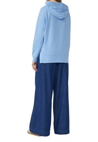 Felpa azzurra chiara con tasca frontale, maniche lunghe e cappuccio grande, abbinata a pantaloni in denim scuro a gamba larga.
