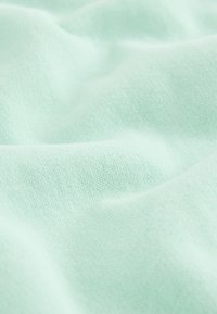 Primer plano de una tela suave de color verde menta claro con textura de punto fina y pliegues suaves que crean sombras sutiles.
