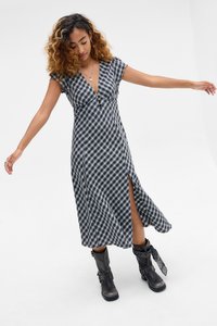 Φόρεμα με ασπρόμαυρο καρό σχέδιο, βαθύ V λαιμόκοψη, κοντά μανίκια και σχίσιμο στο πλάι, συνδυασμένο με μαύρα μποτάκια αστραγάλου και διακοσμητικό φουλάρι.