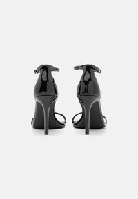 Musta lakattu nahka korkokenkä sandaalit nilkkaremmillä, avointa varvasta muotoilua ja hoikkia stiletto-korkoja, joissa on sileä kiiltävä viimeistely.
