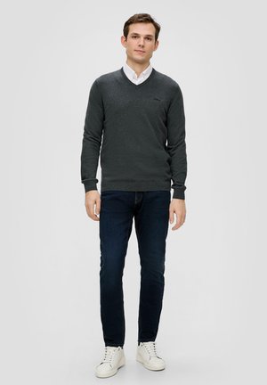 Donkergrijs V-hals trui met lange mouwen, gecombineerd met marineblauwe jeans en witte sneakers. De trui heeft subtiele logo-details.