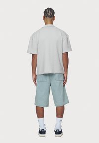 Graues, strukturiertes Kurzarmhemd und hellblaue Jeansshorts. Das Outfit wird mit schwarzen Turnschuhen und weißen Sportsocken komplettiert.