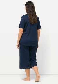 Ensemble de pyjama en coton bleu marine comprenant une chemise à manches courtes et un pantalon court avec un bord en dentelle, texture lisse et coupe décontractée.
