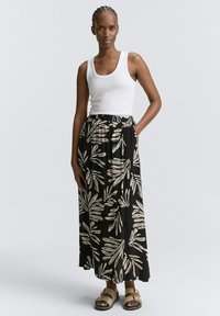 Schwarzer, floraler Maxikleid mit beigen Blättern, aus leichtem Stoff. Kombiniert mit einem weißen Tanktop und braunen Sandalen.