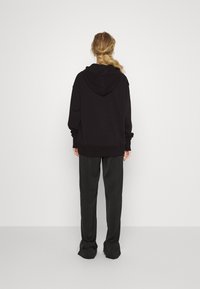 Czarna bluza z kapturem, z dużym kapturem i luźnym krojem, zestawiona z ciemnoszarymi, prostymi spodniami. Tkanina wydaje się być miękka i lekka.