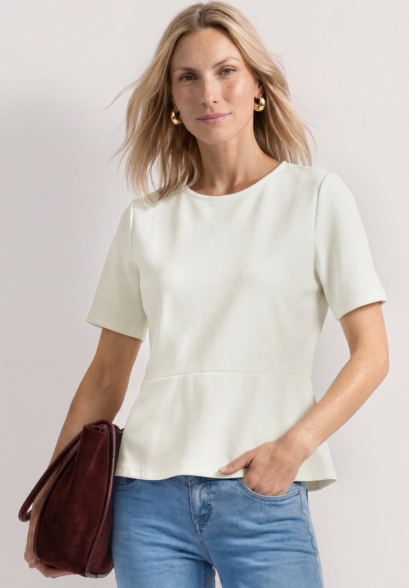 Femme blonde portant un haut blanc à manches courtes et un jean bleu tient un grand sac à main bordeaux avec une main dans sa poche.