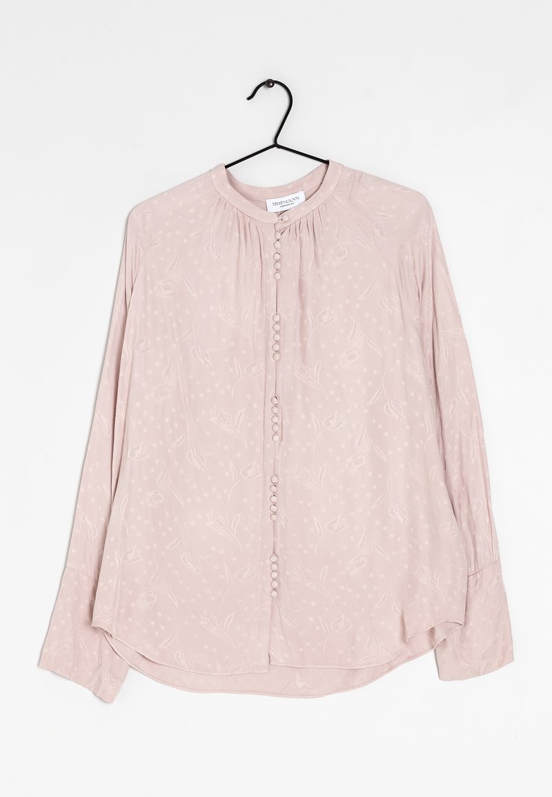 Blouse rose clair à manches longues avec un motif floral et à pois subtil, col rond, boutons recouverts de tissu, suspendue sur un cintre noir.