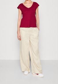 Burgundy V-neck t-shirt with short sleeves paired with cream wide-leg trousers. Outfit completed with white slip-on shoes.