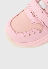 Ροζ αθλητικό παπούτσι με λείο δερμάτινο επάνω μέρος, μοτίβο σε πλέγμα, ιμάντα με κλείσιμο hook-and-loop και ελαφρώς διαφανές καουτσούκ πέλμα.