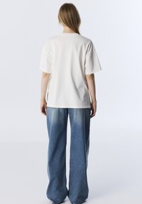 T-shirt bianco in cotone a maniche corte, con collo rotondo e vestibilità rilassata, abbinato a jeans a gamba larga azzurri, con una lavaggio sbiadito.